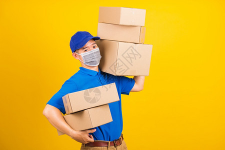 身穿蓝色T恤衫和制服的亚洲年轻送货工人身穿蓝色T恤衫和帽子制服的亚洲年轻送货员身着面罩在冠状或COVID19下身穿面罩背着保护式背景图片