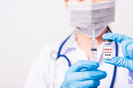 身着制服和手套的亚洲女医生或护士身戴面罩保护在实验室中持有针头注射器药物和瓶疫苗子上都有COVID19VACCINE的文字标签图片