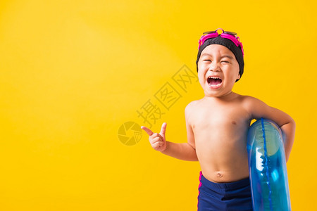 暑假概念肖写亚洲快乐可爱的小男孩穿着护目镜和泳衣握着蓝色充气环基德和哈夫有趣的手指边对摄影棚拍孤立的黄色背景图片