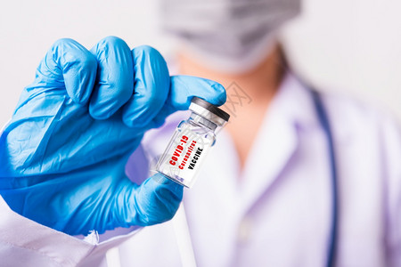 穿制服的女医生或科学家身着面罩在实验室中佩戴保护面罩使用手握的瓶子疫苗在上疫苗贴有CORNAVIRUSVACCINE的文字标签C图片