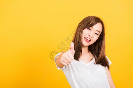 亚洲快乐肖像美丽可爱的年轻女孩站着穿T恤衫展示手指拇仰望摄影机的孤立图片