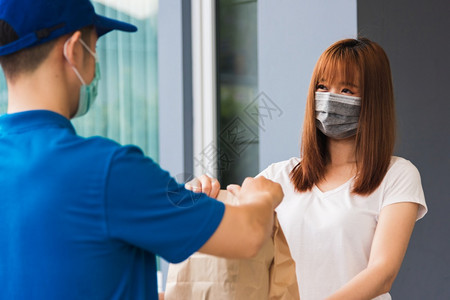 亚洲快送递的年轻男子向接受保护面罩的女客户提供纸袋快餐根据宵禁检疫大流行冠状COVID19进行保护面罩图片
