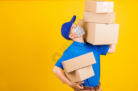 身穿蓝色T恤衫和制服的亚洲年轻送货工人身穿蓝色T恤衫和帽子制服的亚洲年轻送货员身着面罩在冠状或COVID19下身穿面罩背着保护式背景图片