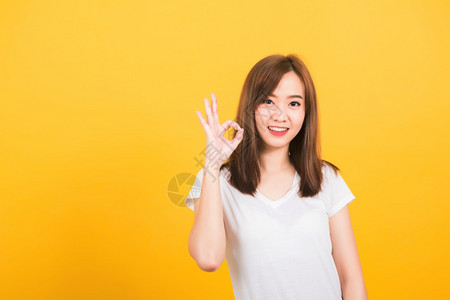 亚洲快乐的肖像美丽可爱年轻女子站着穿T恤衫展示用手指好牌图片