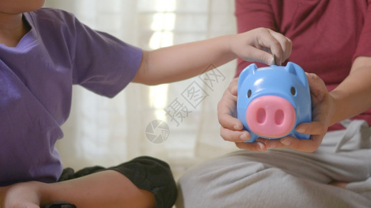 快乐的亚洲男孩学龄前和母亲把硬币放进小猪圈里孩子把硬币放进小猪银行里因为在家存着一堆硬币投资教育概念图片