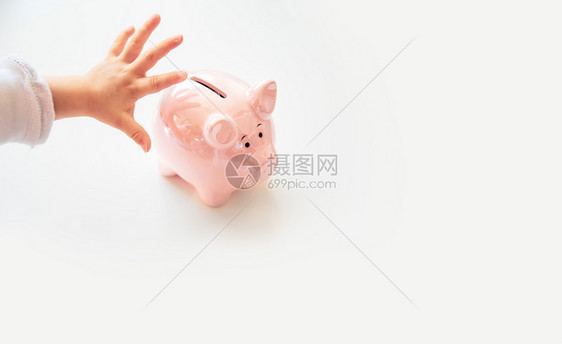 婴儿手在粉红小猪银行中储蓄亮白孤立的背景复制空间文本婴儿手在粉红小猪银行中储蓄图片