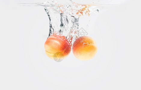 两颗杏子掉入水中在白背景上喷洒和气泡空在白背景上图片