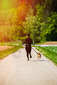运动女孩在春天带着一条狗Beagle跑步在通往森林的农村公路上阳光明媚的一天是阳光明媚的一天复制自然空间运动女孩在农村公路上与一图片