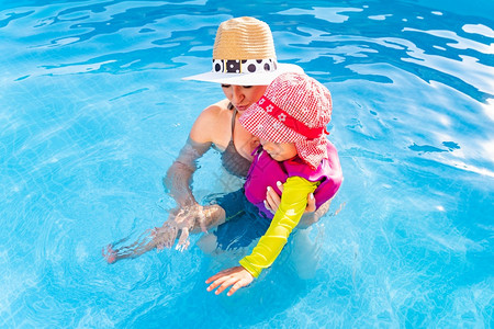 23岁的孩子母亲在游泳池中学习婴儿在池中学习婴儿在池中学会婴儿在家里学会游泳夏季概念图片