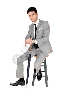 一个英俊高的商人坐在椅子上手里拿着一把伞看摄像机为白色背景而孤立图片