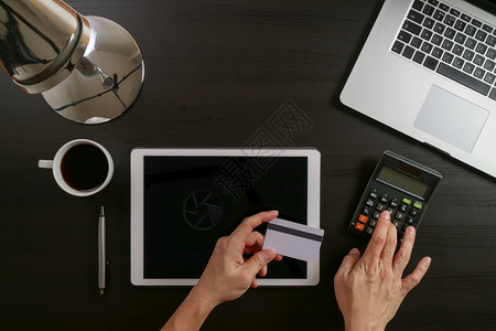 利用笔记本电脑和信用卡及平板电脑在黑木桌背景上工作的手观图片