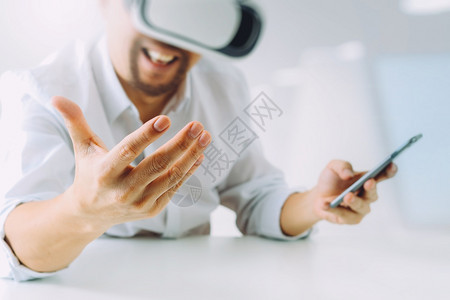 商人在现代办公室佩戴虚拟现实护目镜用智能手机使VR头盔的现代办公室使用智能手机图片