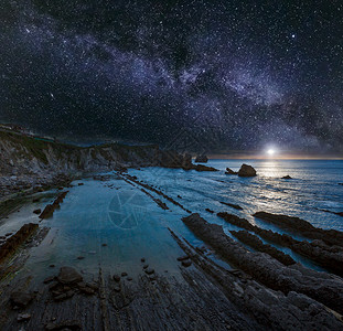 ArniaBeach西班牙大洋沿岸从岩石中夜视月亮和星状银河在天空中升起月光在水中反射图片