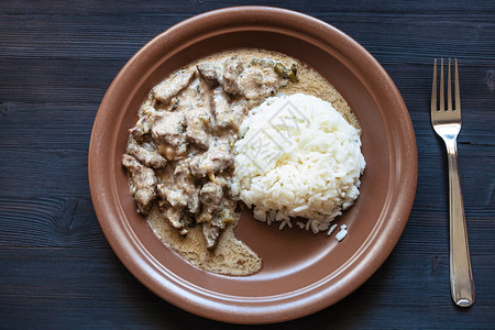 大米黄瓜俄罗斯料理在深色餐桌上的棕色盘子上放上一份牛肉酸奶油炖肉和煮米饭背景