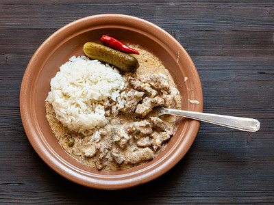 俄罗斯料理在深色桌子上的棕色盘子上用酸奶油和煮米饭炖牛肉片图片