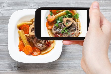 旅行概念智能手机用白色盘子上的意大利餐Osssobuco的游客照片图片