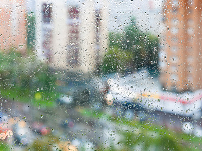 白天的城市秋天雨背景的家用窗户玻璃上的雨滴和模糊街道上背景