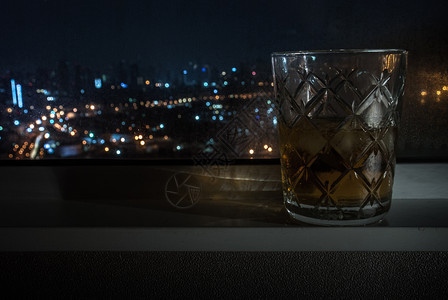 派对大灯威士忌玻璃放在该市旅馆房间窗户旁边有外部观车前灯光照亮了汽车头灯适于制作背景图象供广告使用b于宣传城市背景图片