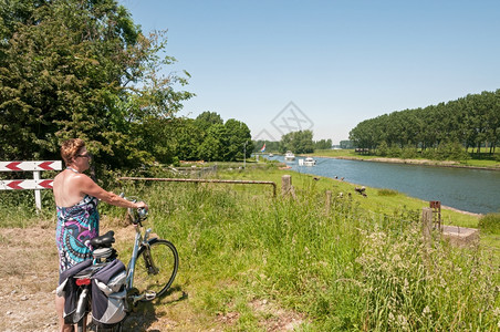 树木站在自行车上着的女人看在荷兰的河上经过船只女士门户14图片