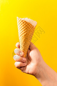 舀食物锥体黄色背景的手握冰淇淋甜筒图片