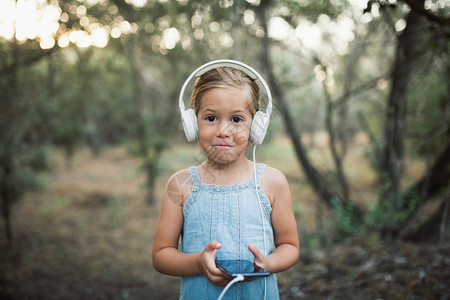 小女孩在森林里用她的智能手机和耳监听音乐请享用金发女郎童年图片