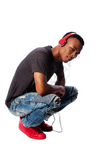 青春期非洲英俊的青少年在蹲着时听穿戴红色耳机的音乐男生牛仔裤图片
