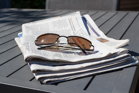 消息书面阅读报纸和太阳镜放在花园的桌子上图片