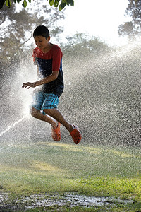 滴孩子洒水器儿童在炎热天气中与喷水的者玩图片