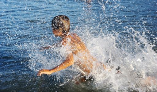 一个男孩在Kinneret湖温水中玩耍溅快乐的晒黑图片