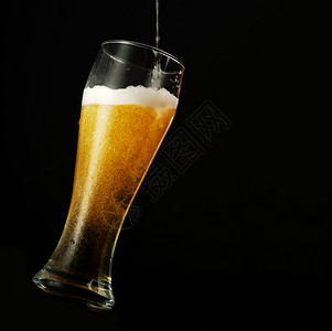 进入酒精将啤倒在玻璃中黑背景上黄色的图片