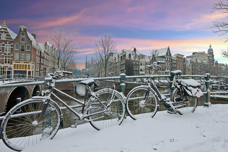 下雪的黄昏建筑学日落时荷兰阿姆斯特丹市中心的雪地自行车图片