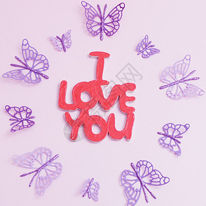 镂空紫色的木雕我爱你在粉红色的背景和紫色纸蝴蝶周围的题词图片
