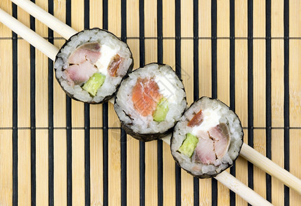 制作三片寿司卷在筷子和竹垫上健康午餐图片