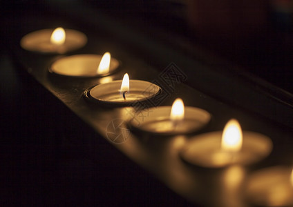 在长蜡烛架上排成一的蜡烛以中心黑暗水平图像为焦点目的白色火图片