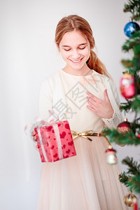 带着圣诞礼物的快乐笑女孩站在树后面一种假期展示图片