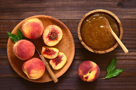 甜的核果食物木碗中的桃果酱或冻边上有木板的新鲜成熟桃子水果用天然光桃子酱或果汁在黑木头上拍摄了相片图片