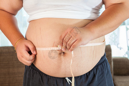 健康人们亚洲胖子在家里拿着一个测量磁带腰部图片