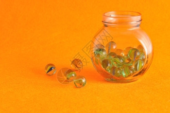 透明玩闪亮的以橙色背景展示的玻璃罐中弹珠集装在玻璃罐中图片