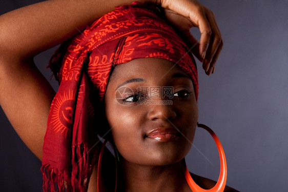美国人身戴传统部落红橙色头巾围和大桔连环耳的美籍黑人女子头顶有胳膊被孤立手臂灰色的图片