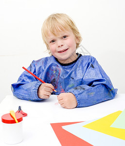 艺术家年轻的俏皮小孩在一张大纸上涂着彩色对镜头微笑图片