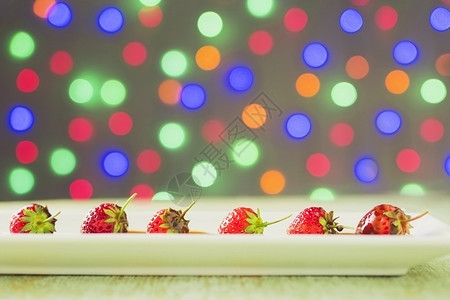 所有的白色盘子里巧克力大衣的草莓超过多彩光浅布基背景糖丰富多彩的图片