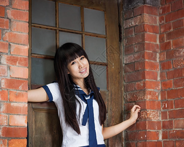 漂亮的亚洲女学生在砖墙旁的门前拍照图片