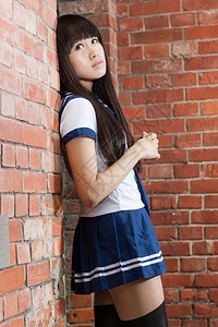 漂亮的亚洲女学生在砖墙旁拍照图片