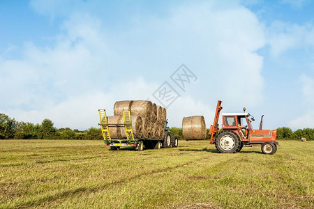 稻草拖拉机在野外收集干草篮子和装上农车手推辆图片