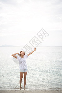 年轻美女站在海滩上赤脚放轻松的节日中举起双臂在空中伸展水女拉紧图片