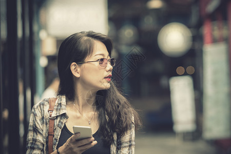 眼镜吸引人的近距离面对着亚裔年轻女在购物区手持智能机的亲行走聊天图片