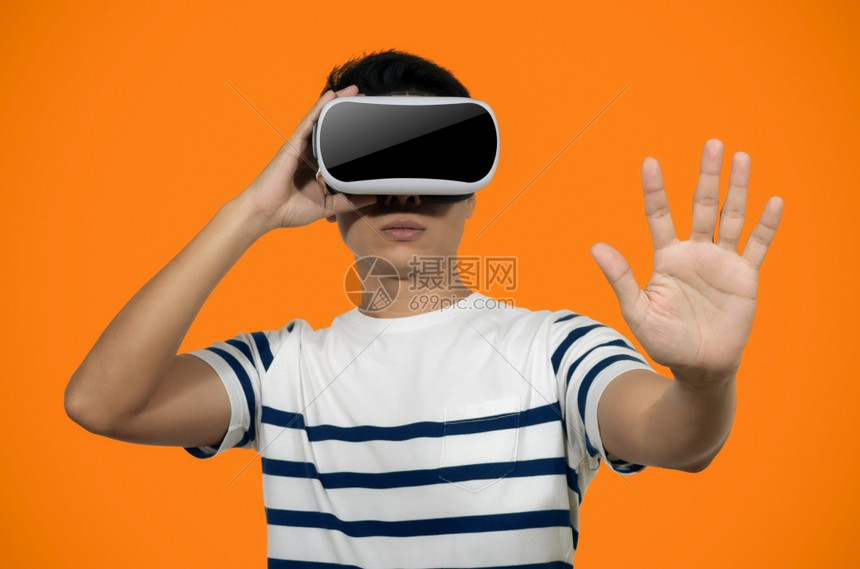 男乐趣有虚拟现实头盔的年轻人站在橙色背景的室内青年拿着虚拟现实头盔的年轻人图片