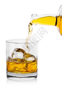 喝不倒翁寒冷的金威士忌从瓶子倒进玻璃冰在白色背景上隔绝的冰黄金威士忌从瓶子倒到杯加冰图片