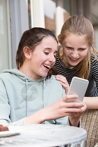 微笑户外社会的两名在咖啡厅年轻女孩通过移动电话阅读短信图片