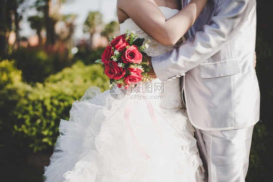 新娘手里握着婚礼红玫瑰花束新郎拥抱娘手中握着婚礼红玫瑰花束新郎拥抱娘在一起的结婚情人概念婚情爱美丽的人类一种图片